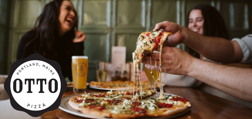 In the foreground, someone is lifting a cheesy slice of pizza from a whole pie, with strings of melted cheese stretching as it’s pulled away. The pizza is thin-crust, topped with tomato sauce, herbs, and cheese. Another pizza is visible on the table. Behind the food, two women are sitting at the table, smiling and laughing, creating a warm, social, and friendly atmosphere. Drinks, including a pint of beer in a branded glass, are also on the table. On the left side of the image is the OTTO Pizza logo, a black-and-white circular design with the words “PORTLAND, MAINE” at the top, “PIZZA” at the bottom, and “OTTO” in bold letters across the center. The photo conveys a casual, inviting dining experience focused on good food and good company.